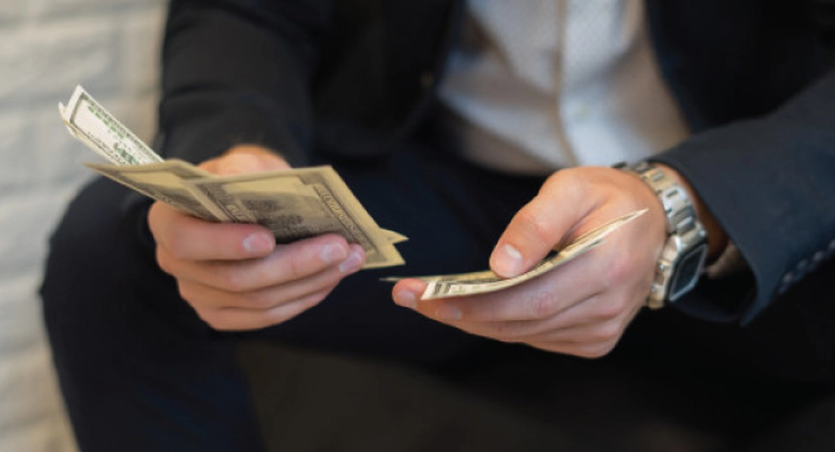 Man in a suit sitting down counting cash