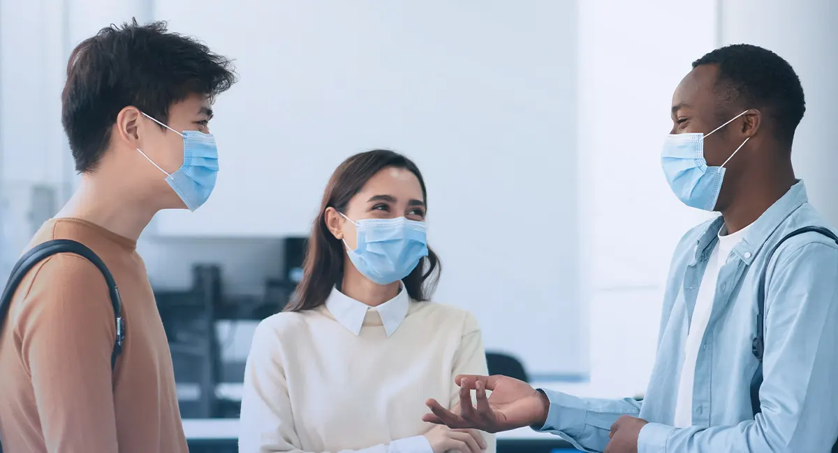 man in protective medical mask and rubber gloves poses in supermarket, holds glass bottle of alcoholic drink, reads label